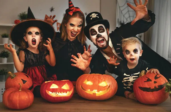 Pessoas fantasiadas em uma sala com aboboras escupidas na mesa durante o hallowen