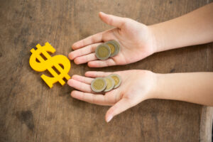 Imagem de capa: uma mão com moedas e ao lado o símbolo do dinheiro.